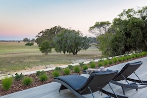 A deck with two lounge chairs and a small table, overlooking a grassy field with trees.