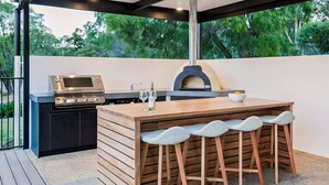 Cozinha externa com churrasqueira, forno a pizza e banquetas de bar.