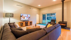 Ein modernes Wohnzimmer mit großem Fernseher, Kamin und Blick ins Freie.