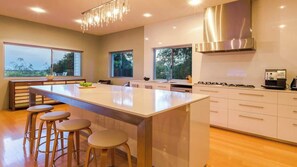 A modern kitchen with a large island, bar stools, and a stainless steel range hood.
