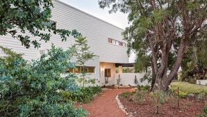 Uma casa moderna com um caminho que leva à entrada, rodeada por diversas plantas e árvores.