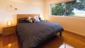 Um quarto com cama, mesas de cabeceira, uma janela com vista e um termostato na parede.