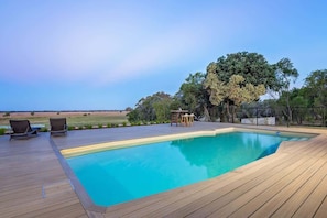 Ein rechteckiger Swimmingpool mit Holzterrasse, zwei Liegestühlen und einem kleinen Tisch.