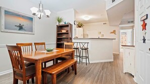 A dining area with a wooden table and chairs, a kitchen with a white countertop, and a 'WELCOME' sign on the door. - Fully Furnished 3 bedroom condo close to the beach and pier (Saint Simons Island)