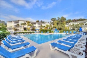 A swimming pool with lounge chairs, a building with balconies, and surrounding greenery.