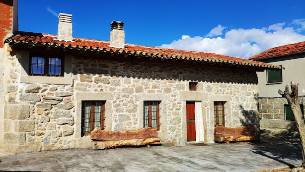Un edificio de piedra con techo de tejas, varias ventanas y un banco de madera al frente.