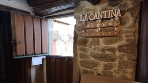 Un interior rústico con pared de piedra, contraventanas de madera y un cartel que dice "LA CANTINA".