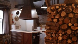 Una cocina rústica con pared de piedra, armarios de madera, un microondas y una pila de leña.