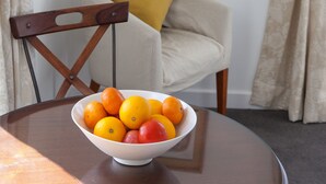 Une table à manger avec un saladier de fruits, une chaise en bois, un coussin et un tableau encadré accroché au mur.