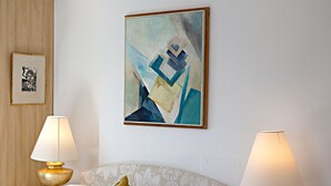 Une chambre d’hôtel avec un lit, deux lampes de chevet, un oreiller, un tableau abstrait encadré et une photographie encadrée accrochée au mur.
