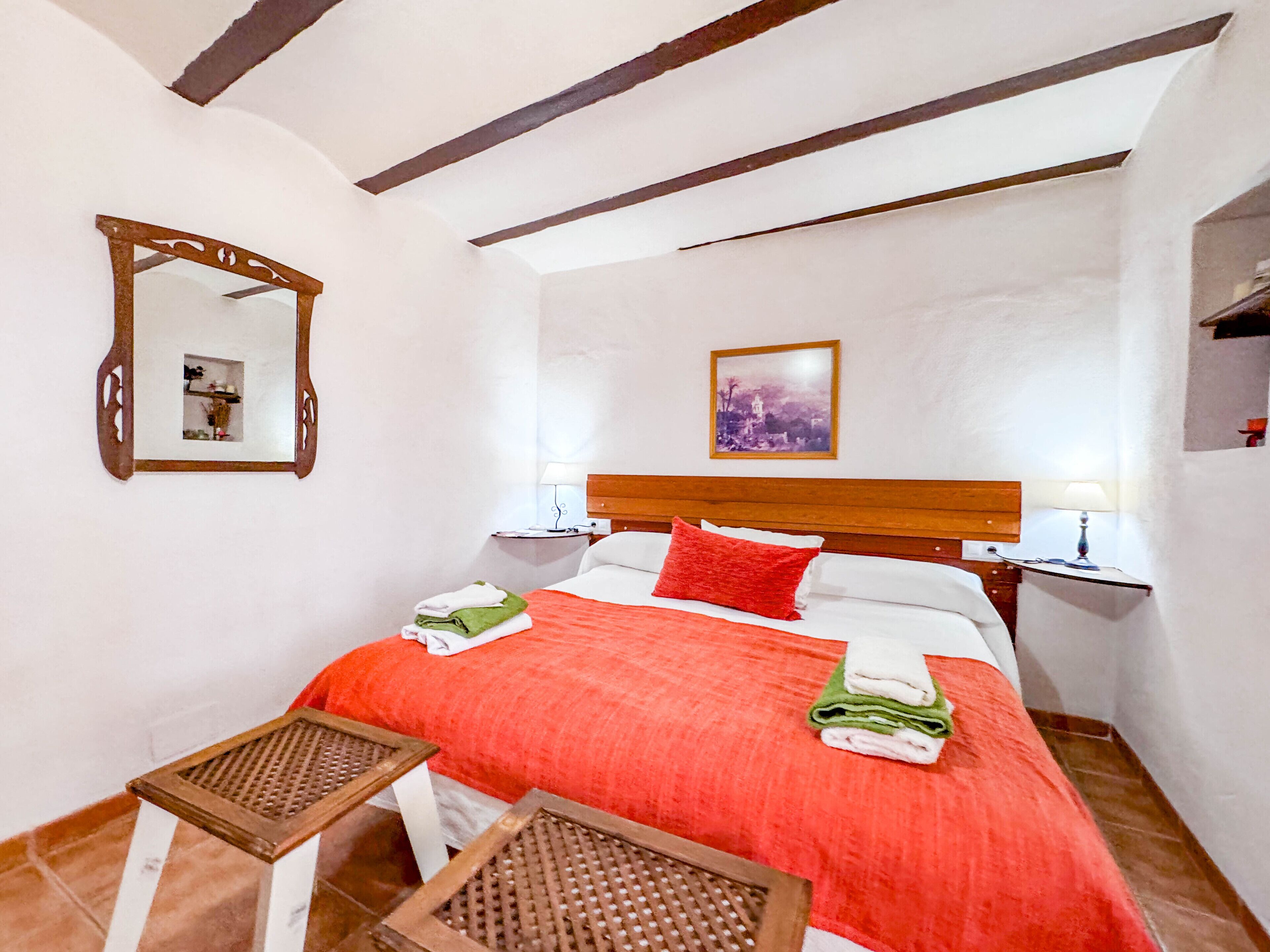 Habitación de hotel con cama, dos mesitas de noche, un espejo, un cuadro en la pared y una pequeña mesa.