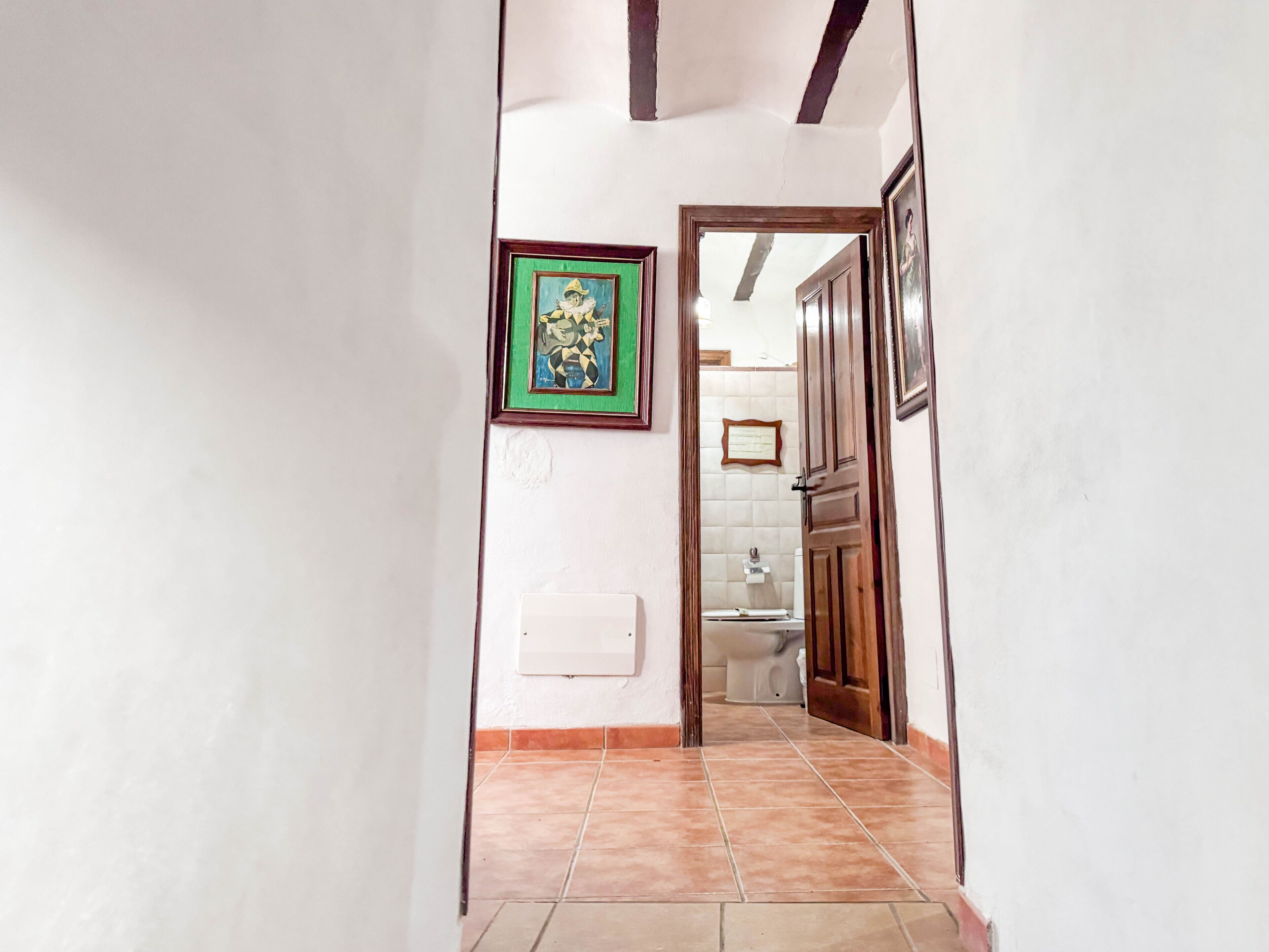 A hallway with a tiled floor, a framed picture on the wall, and a door leading to a bathroom.
