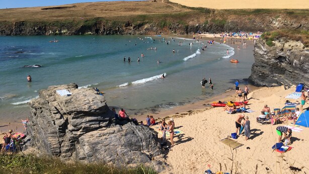 Ein Strand mit felsigen Klippen, klarem, blauem Wasser und Menschen, die den Strand und Wassersportarten genießen.