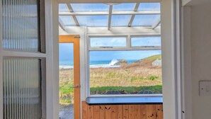 Blick aus einem Zimmer mit großem Fenster auf eine Küstenlandschaft, einschließlich Wellen und einer Felsformation.