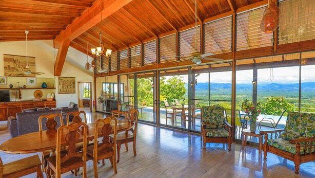 Un vaste espace dédié à la salle à manger, avec une grande table et des chaises en bois, un coin cuisine équipé d’appareils modernes, et de grandes fenêtres offrant une vue sur le paysage.