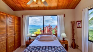Une chambre à coucher avec un lit, un plafond en bois, une fenêtre avec des rideaux et une vue sur la verdure.