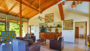 Un salon spacieux avec des canapés en cuir, un plafond en bois et une grande fenêtre donnant sur un paysage verdoyant.