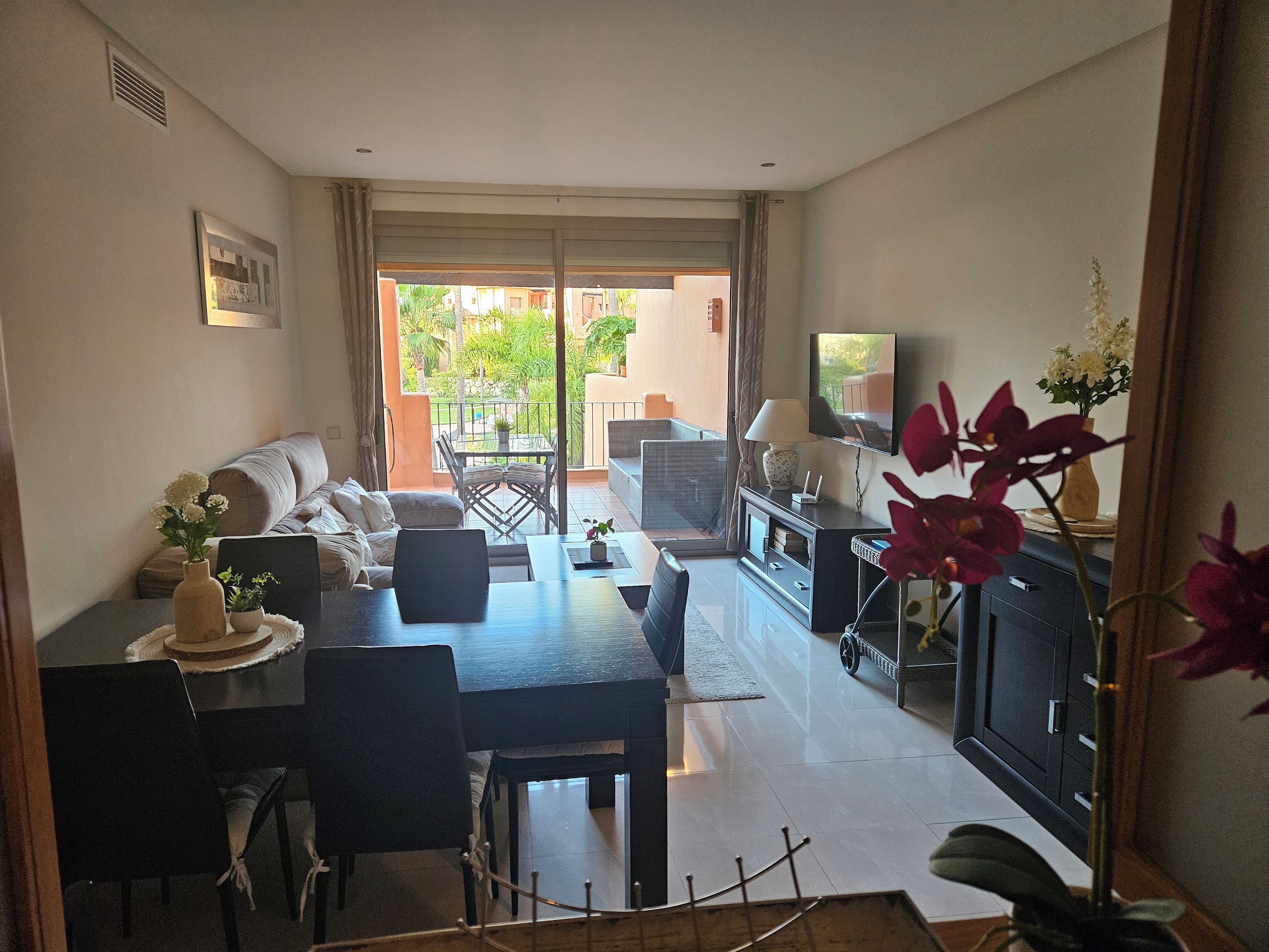 A living room with a sofa, dining table, chairs, a TV, and a balcony with outdoor furniture.