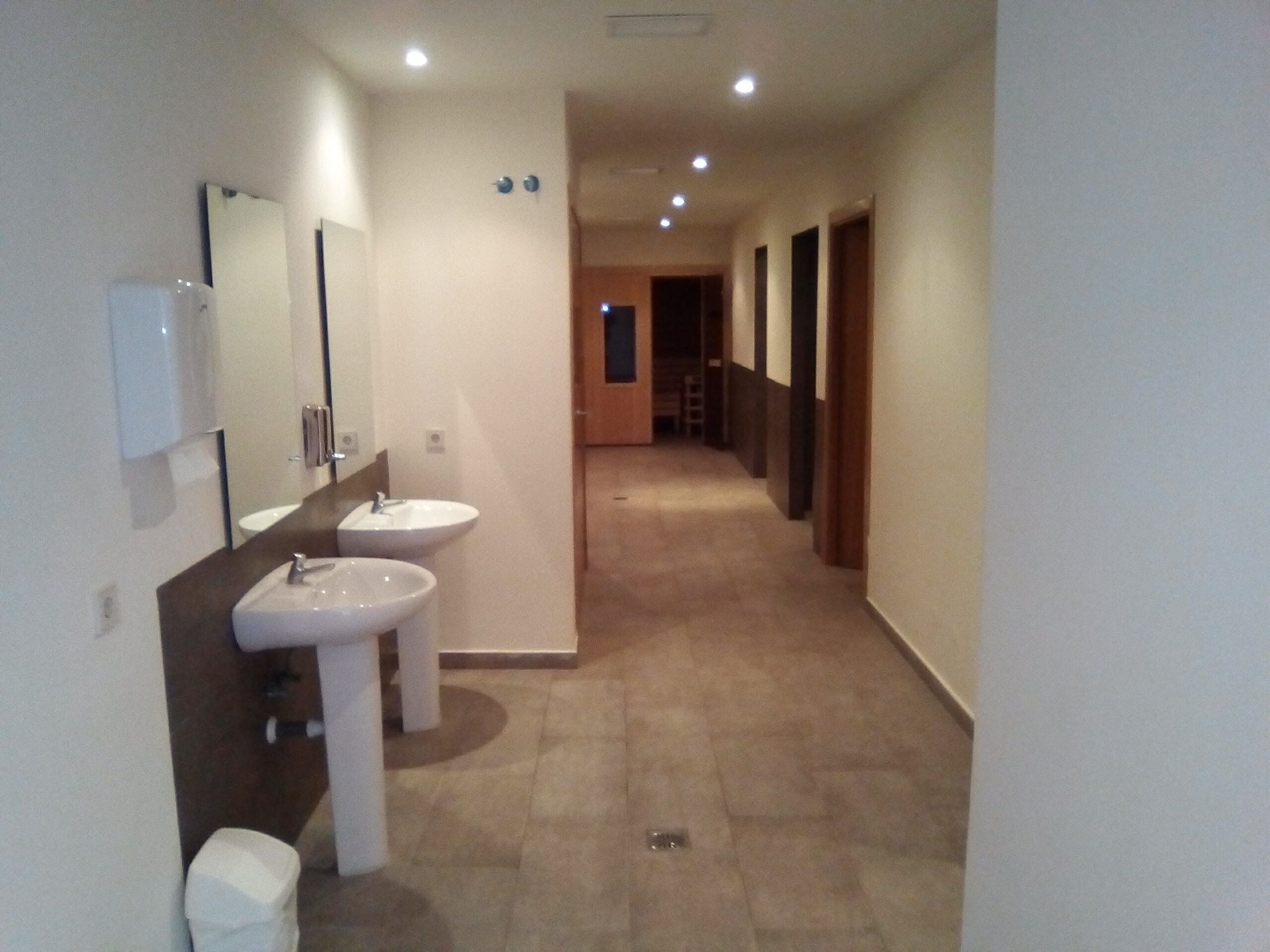 Un couloir étroit avec deux lavabos blancs et un miroir sur le mur de gauche.