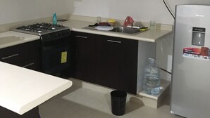 Een kleine keuken met donkere kastjes, een gasfornuis, een magnetron en een koelkast.