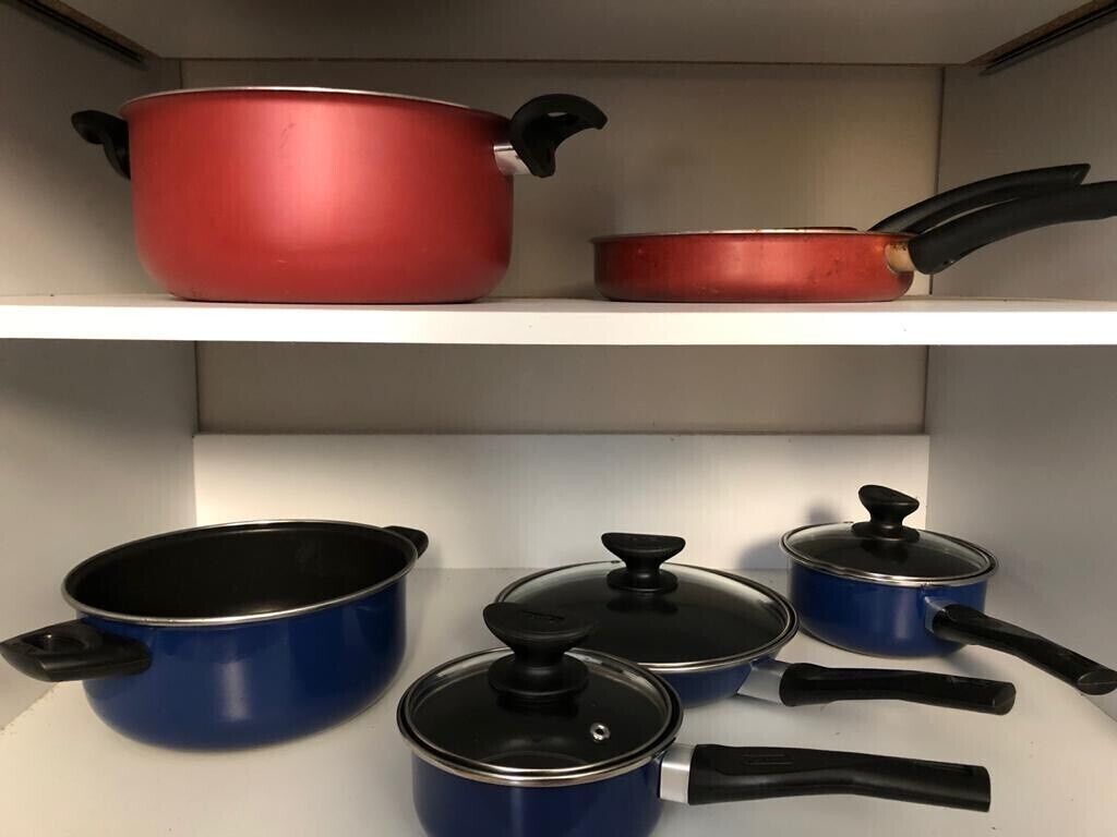A kitchen shelf with various pots and pans, including a red pot and several blue pots with lids.