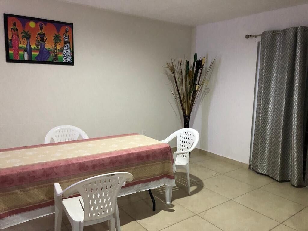 A dining area with a table and chairs, a painting on the wall, and a curtain.