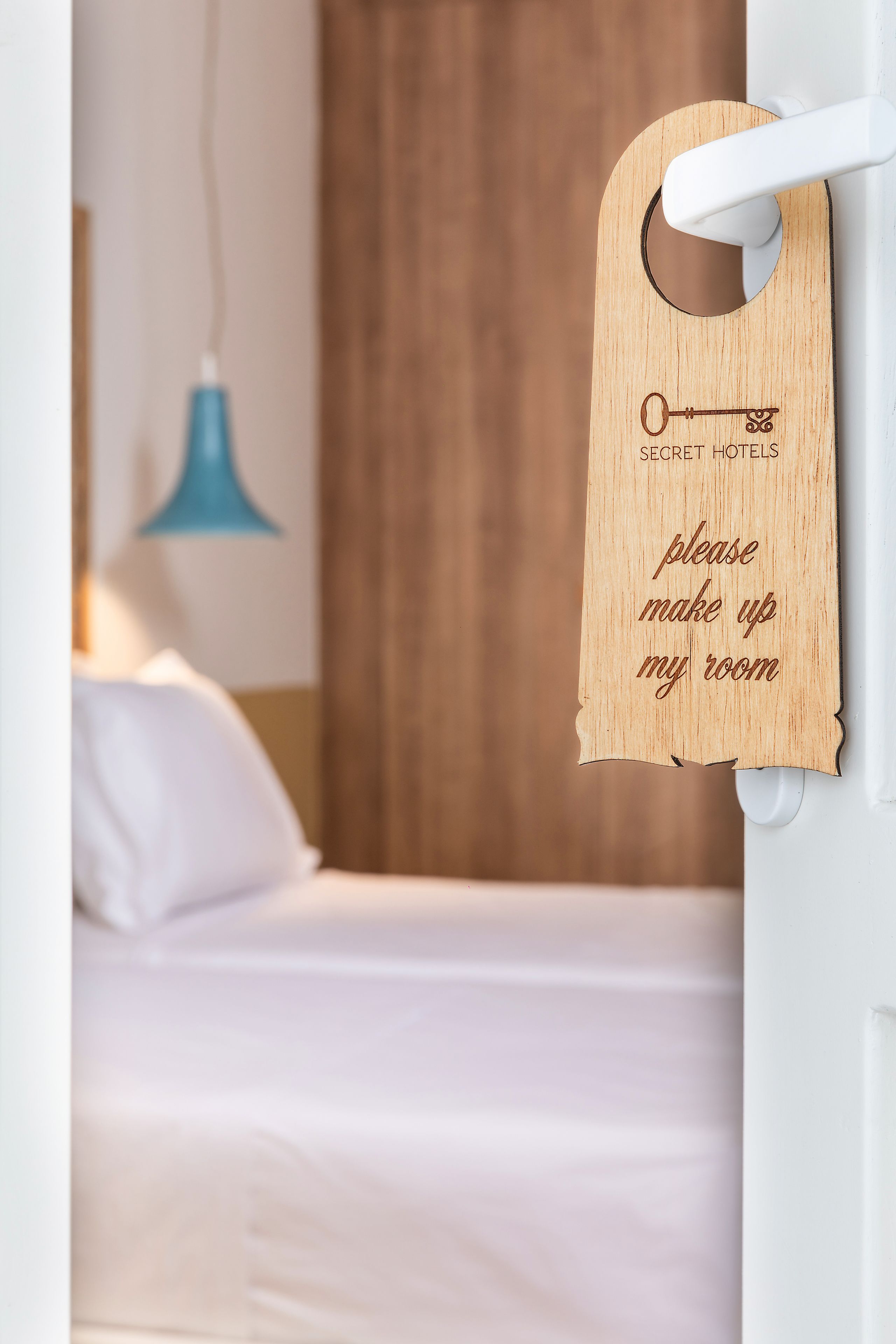 A wooden key-shaped sign with the text "please make up my room" hanging on a white door.