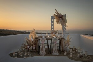 An outdoor wedding setup with a table, chairs, candles, and floral decorations against a scenic backdrop. - Secret View Hotel (Santorini)