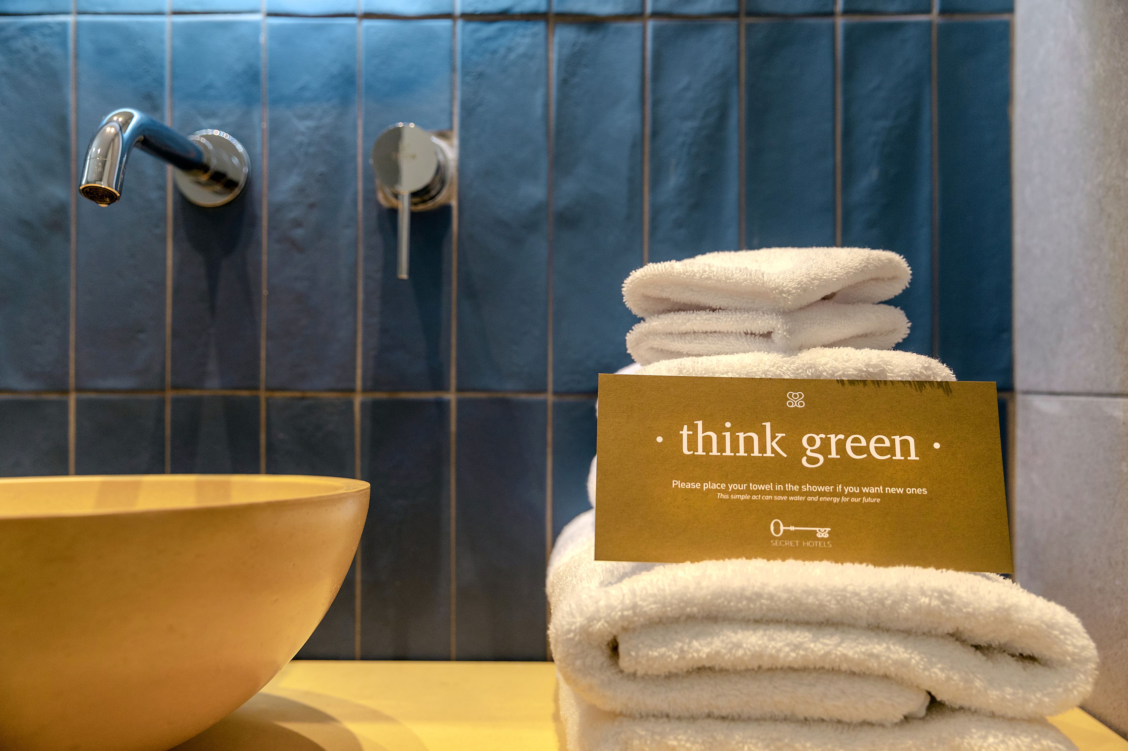 A bathroom with a sink, a towel stack, and a sign that reads "think green."