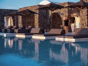 A pool area with lounge chairs and umbrellas, stone walls, and a clear sky.