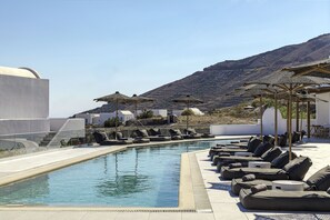 A poolside area with lounge chairs and umbrellas, a clear sky, and a mountainous backdrop. - Secret View Hotel (Santorini)