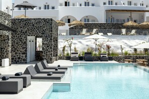 A pool area with lounge chairs, umbrellas, and a stone wall. - Secret View Hotel (Santorini)