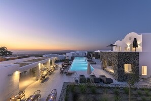A rooftop pool area with a view of the sunset, outdoor seating, and a stone structure. - Secret View Hotel (Santorini)