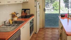 A kitchen with a sink, stove, oven, and refrigerator. There is a window with blinds and a view of greenery outside.