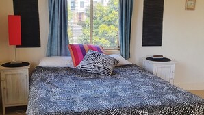A bedroom with a patterned bedspread, a bedside table with a lamp, and a window with curtains.