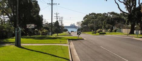A quiet suburban street with a grassy median, utility poles, and a distant view of a body of water.