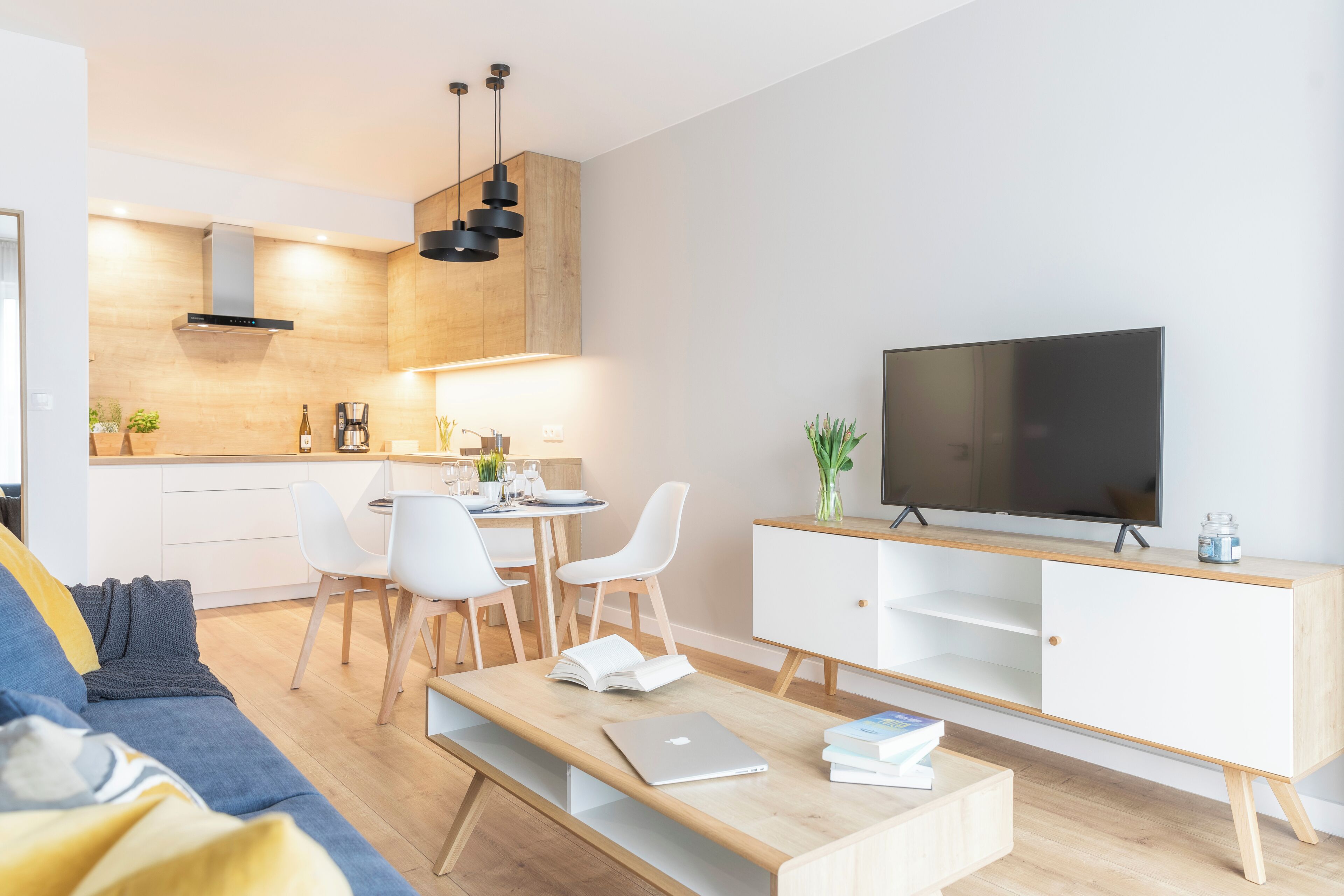 A modern living room with a sofa, coffee table, TV, dining area, and kitchen.