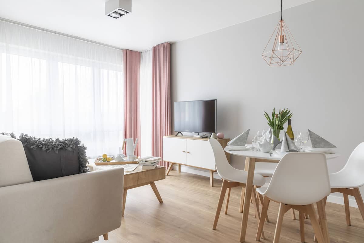 Una sala de estar moderna con un sofá, una mesa de comedor con sillas, un televisor y una lámpara colgante.