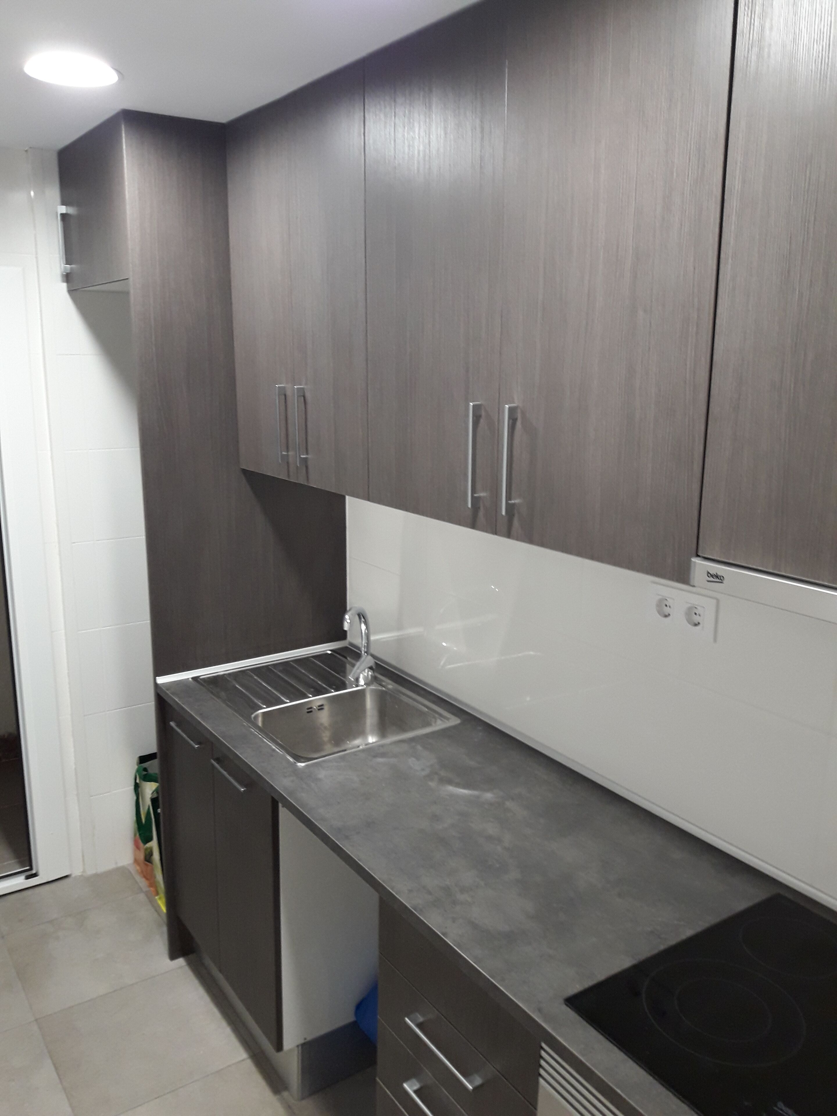 Een moderne keuken met donkere kastjes, een roestvrijstalen spoelbak en een ingebouwde kookplaat.
