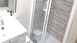 Ein modernes Badezimmer mit einer Glaskabine zur Dusche, einem weißen Waschbecken und einer gefliesten Wand.