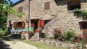 A stone building with a gravel path, wooden shutters, and outdoor seating.