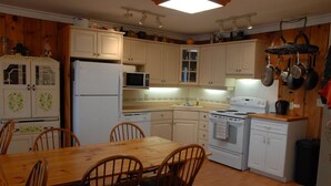 Une cuisine compacte avec des meubles blancs, un réfrigérateur, un four à micro-ondes, une cuisinière et une table à manger avec des chaises.