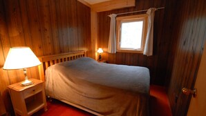 A wooden room with a bed, two bedside lamps, a window with curtains, and a door. - Muskoka Cottage with a Sandy Beach (Baysville)