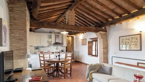 Un interior rústico con vigas de madera a la vista, una zona de comedor con mesa y sillas, un sofá y una cocina al fondo.