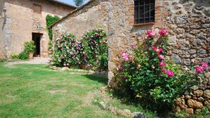 Un edificio de piedra rústico con un pequeño jardín con rosales rosados.