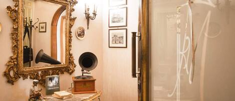 Una habitación con espejos dorados ornamentados, un gramófono y cuadros en la pared.