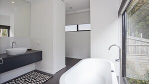 A modern bathroom with a freestanding bathtub, a large mirror, and a dark-toned vanity.