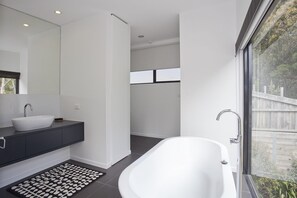 A modern bathroom with a freestanding bathtub, a large mirror, and a dark-toned vanity.