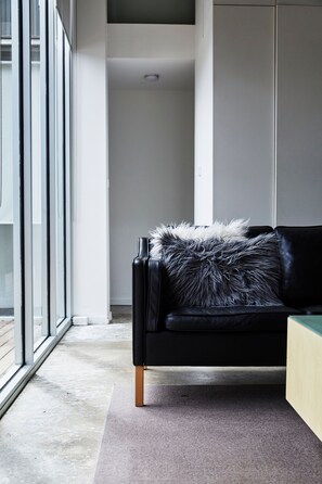 A modern living room with a black leather sofa, a fur throw, and a view through large glass doors. - The Shed Great Ocean Road (Lorne)