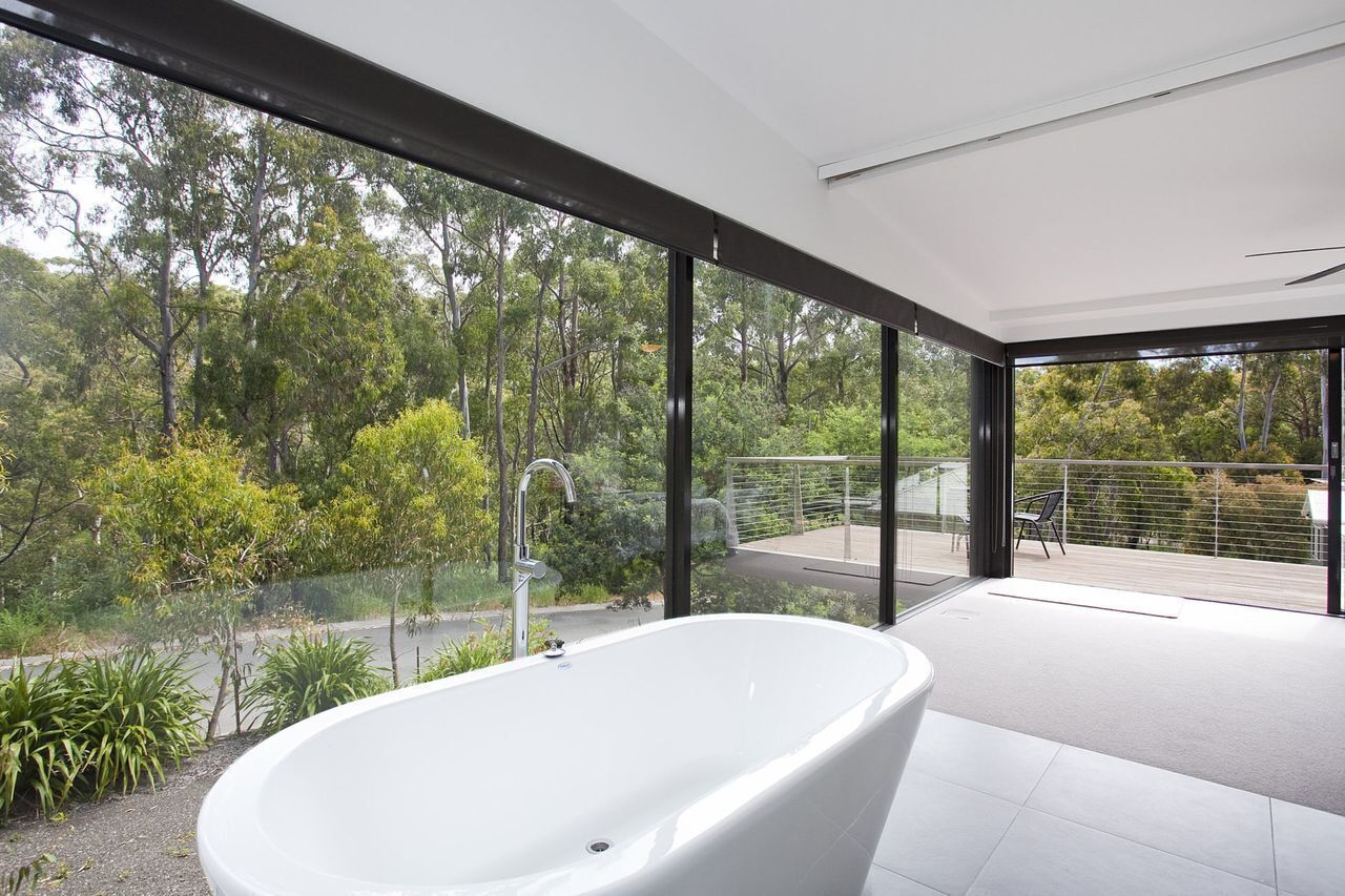 A modern bathroom with a freestanding bathtub, large windows, and a view of a forested area.